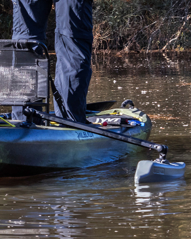 Person standing in a kayak on a body of water with equipment.